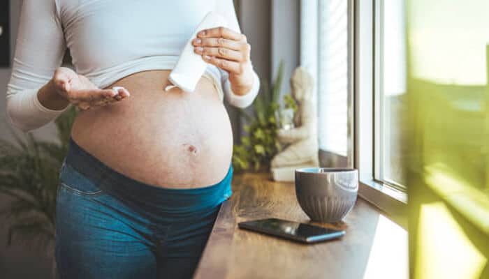 Ingredients to look for and to avoid - tycoonstory | tycoonstory media Pregnant woman using ointment for stretch marks postpartum while standing by a window, applying moisturizer to nourish and prevent skin stretching.