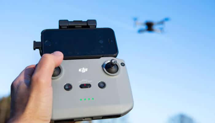 Dji mimo for pc. Person holding a dji remote controller with a smartphone attached while flying a drone, illustrating a setup often managed alongside dji mimo for pc.