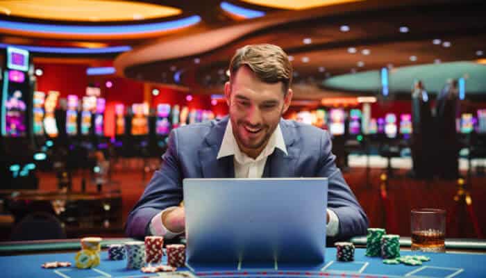 Premium game selection 1 | tycoonstory media Man playing online games at a casino table with chips and a laptop, representing the premium gaming experience offered by squeenvip.