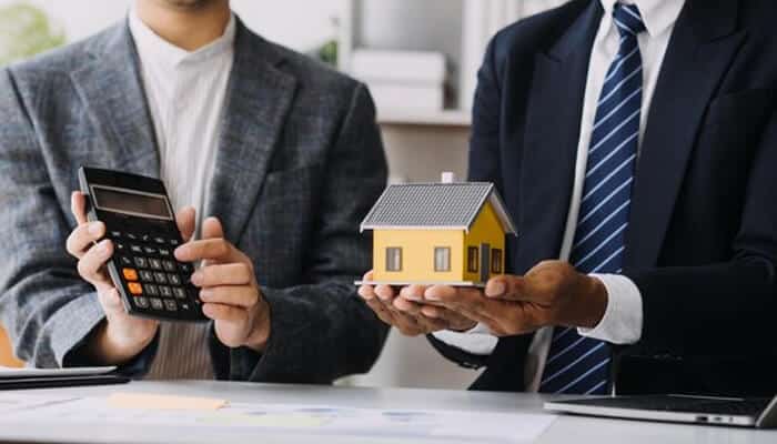Put depreciation to work | tycoonstory media Two property investors discussing over a model house and a calculator, illustrating the decision-making process and calculations involved in property investors.