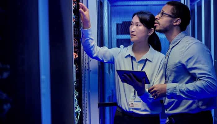Dedicated server Two it professionals inspecting network cables and hardware inside a server room, symbolizing the monitoring and management of a dedicated server environment.