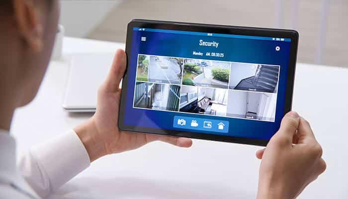 Security systems A person viewing live feeds from multiple security cameras on a tablet, showcasing the modern capabilities of security systems for real-time monitoring.