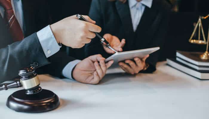 Henderson & henderson Two attorneys from henderson & henderson discussing a case while reviewing information on a tablet, with legal documents and a gavel on the desk.