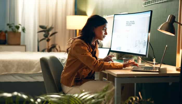 Digital marketing and online strategy services | tycoonstory media A woman working from home during the remote work era, using a laptop and a large desktop monitor to manage her tasks. The cozy room features plants and soft lighting, reflecting the modern shift to flexible work environments.