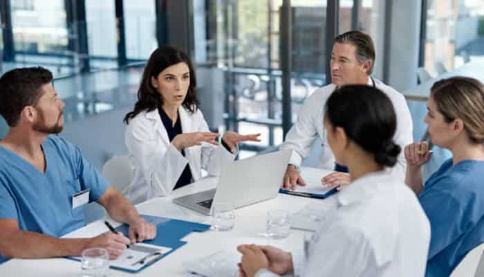 Payers denial algorithms A group of medical professionals seated around a table discussing data on a laptop, illustrating a collaborative review of payers denial algorithms to reduce claim denials and improve healthcare workflow.