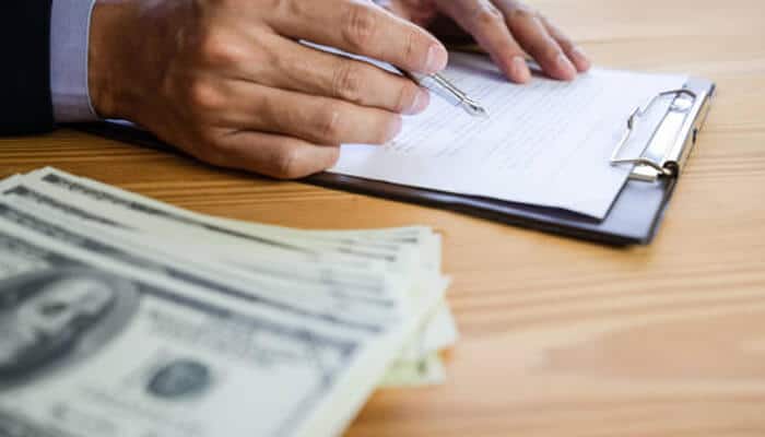 Predatory lending A person signing documents on a clipboard beside a stack of cash, representing the risky agreements often associated with predatory lending.
