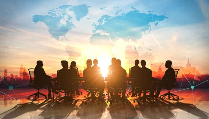 Salman shahid’s Silhouettes of people in a conference room during sunset, with a world map in the background, representing salman shahid’s global business meeting concept.