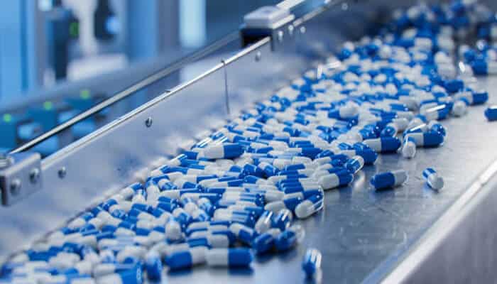 Pill fatigue Blue and white capsules moving along a pharmaceutical production conveyor belt, symbolizing mass medication use and the issue of pill fatigue among patients.