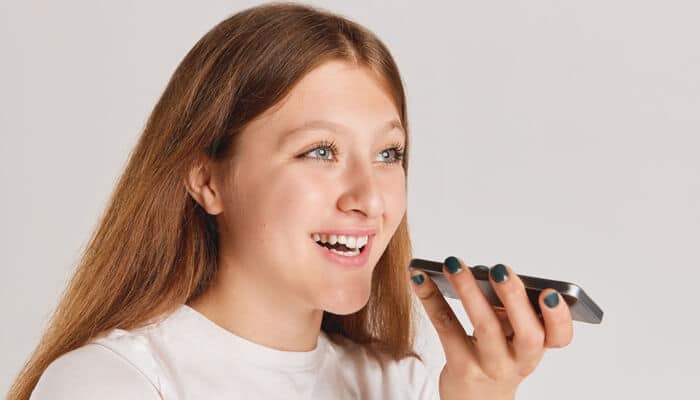 Trust | tycoonstory media A young woman smiling while speaking into her smartphone, illustrating building trust through voice communication and natural, user-friendly voice interactions.