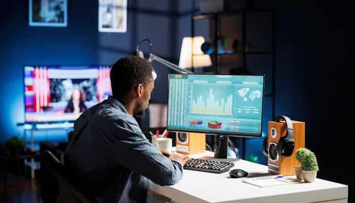 Thumbnail styles A content creator working at a desk with dual monitors, one showing analytics and charts, representing different thumbnail styles and data-driven design choices for digital and video content.