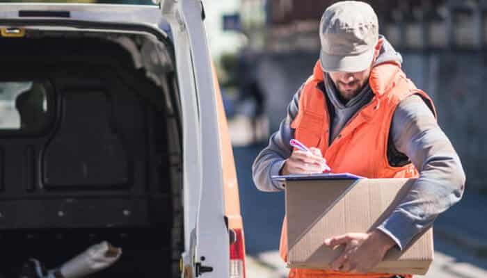Accidents involving independent contractors | tycoonstory media A delivery driver, dressed in an orange safety vest, carefully signs off on a package outside his van, ensuring that everything is in order and that he is a delivery driver enough to handle the task with precision.