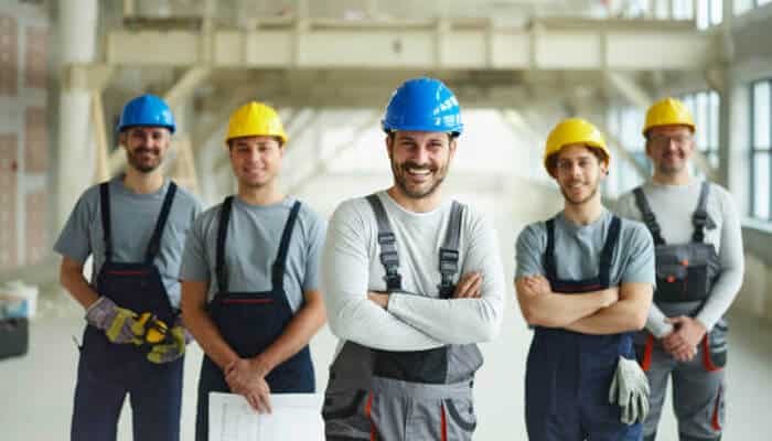 Gold coast’s labour hire industry Group of smiling construction workers wearing safety helmets and work overalls, standing confidently inside an industrial building, representing teamwork and professionalism in gold coast’s labour hire industry.