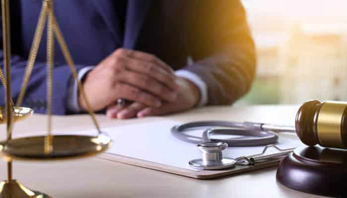 How pharmaceutical negligence redefines corporate risk 1 | tycoonstory media An image of a lawyer’s hands resting on a table, with a stethoscope, gavel, and legal scales in the frame, symbolizing the intersection of law and healthcare, with a focus on the serious issue of pharmaceutical negligence.