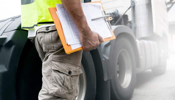 Insurance complexity and delayed responsibility | tycoonstory media A worker holding a clipboard near a commercial truck, highlighting the importance of safety and documentation in commercial trucking accidents for proper claims handling.