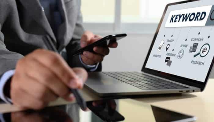 Online marketing gurus Close-up of a marketer using a smartphone and laptop displaying keyword research and seo icons, illustrating data-driven strategy by online marketing gurus.
