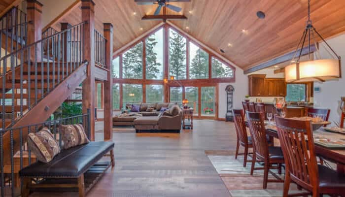 Open-concept living spaces in log cabin | tycoonstory media Open-concept living and dining area inside a modern log cabin, showcasing vaulted wood ceilings, large windows, and rustic interiors that reflect current log cabin design trends.