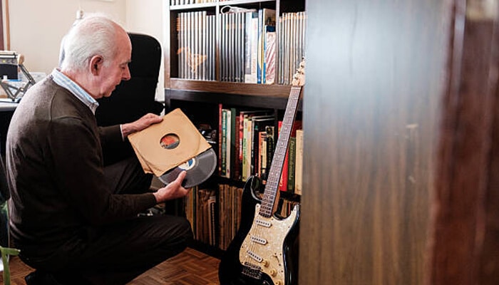 The role of environmental control in preserving vinyl records | tycoonstory media Vinyl records enthusiast browsing classic albums beside bookshelf and electric guitar in cozy music room.