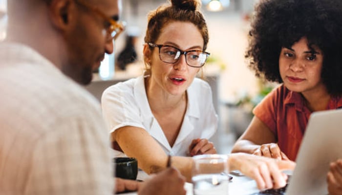 Vending machine business_tycoonstory media | tycoonstory media A group of three people discussing ideas while looking at a laptop, collaborating on a project related to launching a vending machine business.