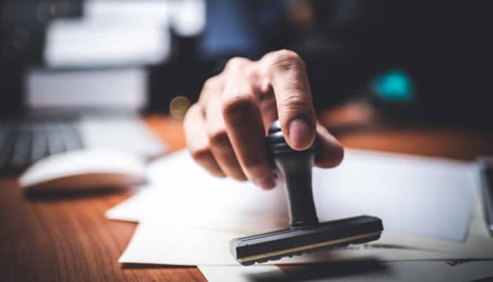 Vending machine business_tycoonstory media | tycoonstory media A hand stamping an'APPROVED' mark on a document, symbolizing the approval process for a vending machine business proposal.