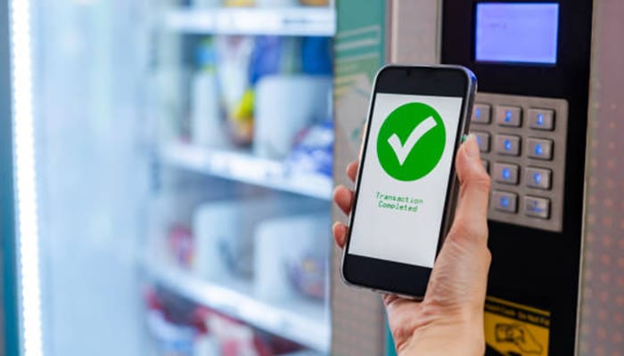Vending machine business_tycoonstory media | tycoonstory media "a person holding a phone with a'Transaction Completed' message while using digital payment at a vending machine, showcasing modern technology in the vending machine business.