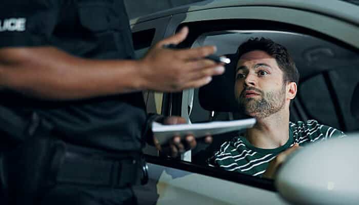 What happens during a dwi arrest | tycoonstory media Police officer speaking to a driver inside a car window during a suspected dwi arrest traffic stop at night.