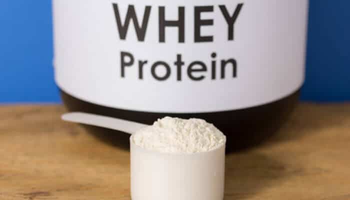 Whey-based protein shakes | tycoonstory media A close-up of a scoop of whey protein powder next to a protein container, highlighting the best protein shakes for muscle growth.