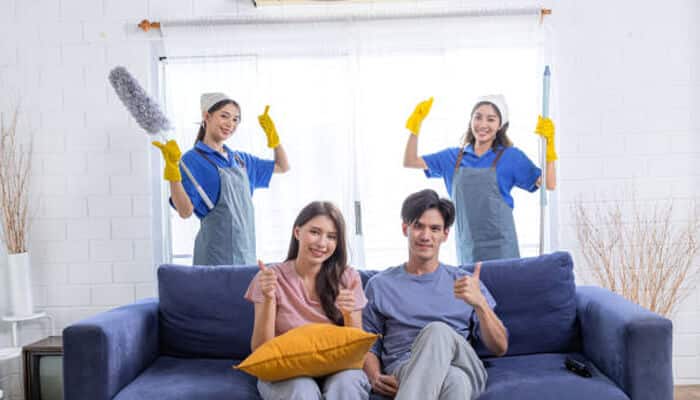 Why do people leave positive reviews for biohazard cleaning | tycoonstory media Residential cleaning crew with equipment standing behind satisfied homeowners on a sofa, representing safe and professional biohazard cleaning services.