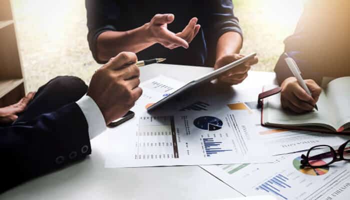 A return to foundational principles | tycoonstory media Business professionals reviewing financial charts and documents during a meeting, discussing investment strategies and private credit opportunities on a tablet and printed reports.