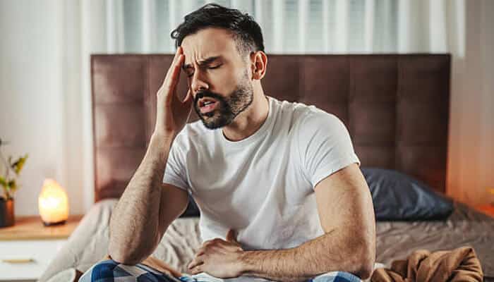 Behavioral and health changes linked to alcohol use | tycoonstory media Man sitting on the edge of a bed holding his head in discomfort, showing visible distress and fatigue—an image illustrating possible warning signs of health or behavioral concerns.
