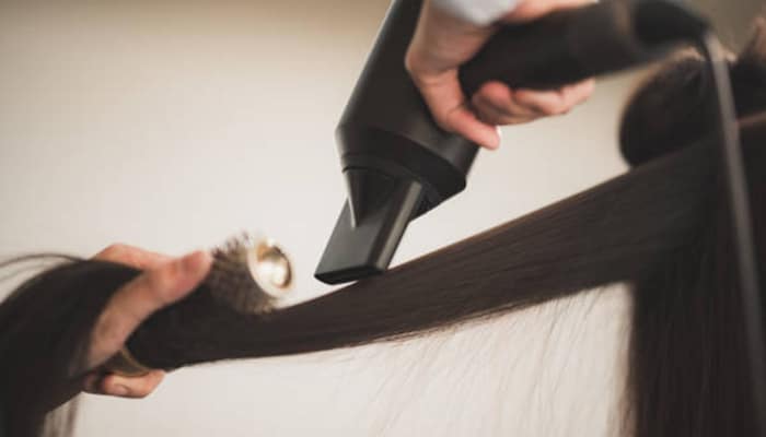 Blow-drying guide | tycoonstory media A person using a blow dryer on fine hair with a round brush to create volume and texture, demonstrating key techniques from this blow-drying guide.