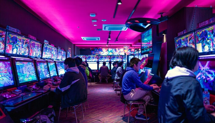 Casino | tycoonstory media People playing arcade-style gaming machines in a brightly lit gaming lounge with neon lights, representing an immersive online gaming experience like mrcoin88.