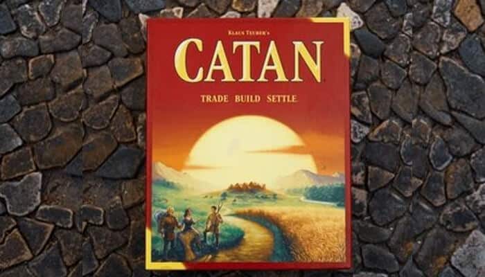 Catan | tycoonstory media The catan board game box featuring the tagline "trade, build, settle," set against a backdrop of stones. A popular choice among board games for families, offering strategic fun.