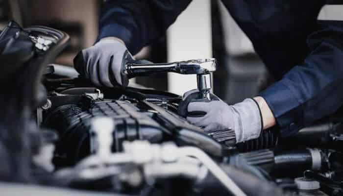 Engine and transmission health indicators | tycoonstory media A mechanic working on the engine of a car using a wrench. Regular maintenance and checks on the engine and transmission are crucial for the longevity of a used suv.