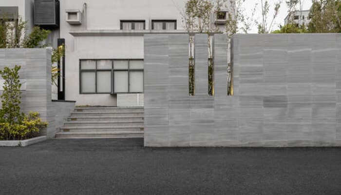 Gate pillar tiles | tycoonstory media Modern entrance with a sleek wall design and steps, featuring stylish outdoor floor tiles that complement the minimalist aesthetic of the space.