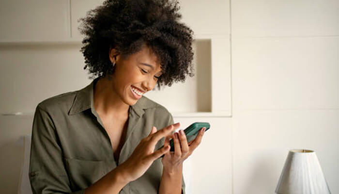 How to identify rebate opportunities | tycoonstory media A woman smiling while using her phone to manage tasks, likely including online electricity bill payments, as she enjoys the convenience of digital solutions for everyday needs.