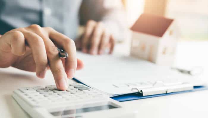 How to use a home loan eligibility calculator properly | tycoonstory media Person using a calculator to determine their home loan eligibility, with paperwork and a small house model in the background, showcasing the process of using a home loan eligibility calculator.