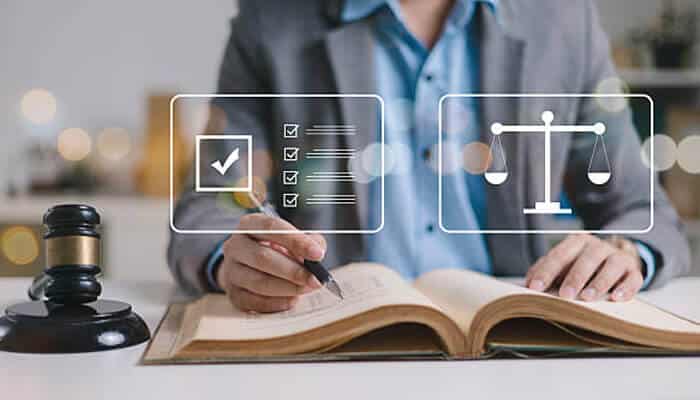 Legal setup checklist | tycoonstory media A person in a suit writes in a legal book with a gavel beside them, accompanied by digital icons of a checklist and scales of justice, symbolizing creating a business plan.