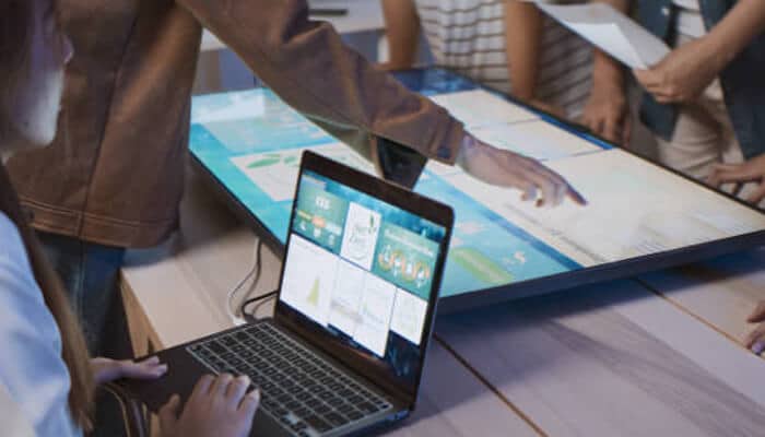 Long-term improvements in recycling rates drive investment | tycoonstory media People collaborating around a large touch screen and laptop, illustrating how technology can aid in recycling businesses by improving efficiency and data analysis.