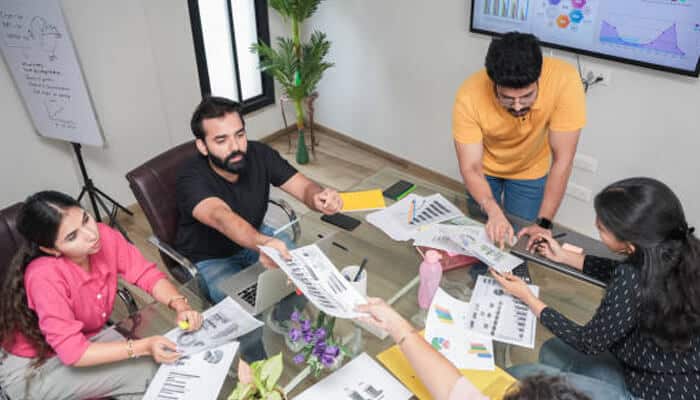 Practical applications for growing startups | tycoonstory media Team collaborating on reports with a background screen showing data, highlighting the use of ai video generation in business strategies.