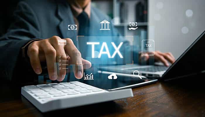 Professional services | tycoonstory media Business professional using a calculator and laptop with a digital “tax” interface overlay, illustrating financial planning and tax deductions management for businesses.