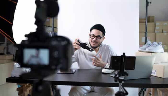 Standardized grooming details | tycoonstory media Man filming a product review video while showcasing a shoe at a desk setup, highlighting subtle style choices in fashion content creation with professional camera equipment and light