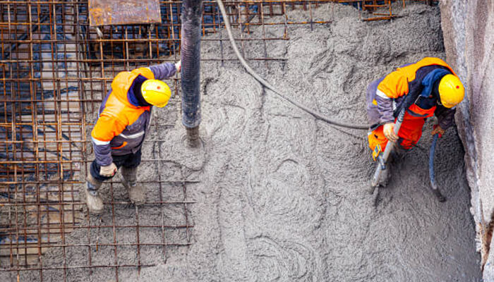 Striking the perfect balance with time | tycoonstory media Workers in safety gear pouring concrete onto a construction site, preparing the surface for concrete foundations. The image showcases the essential process of building strong, durable foundations.