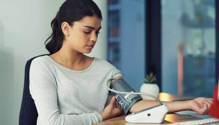 The critical role of managing blood pressure | tycoonstory media A woman monitoring her blood pressure at a desk, highlighting the importance of managing blood sugar, blood pressure, and cholesterol for overall health.