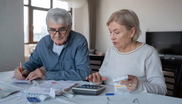 Understanding how fd rates affect retirement income | tycoonstory media An elderly couple reviewing financial documents and using a calculator, considering their investments. Understanding fixed deposit rates for senior citizens is key to maximizing retirement income.