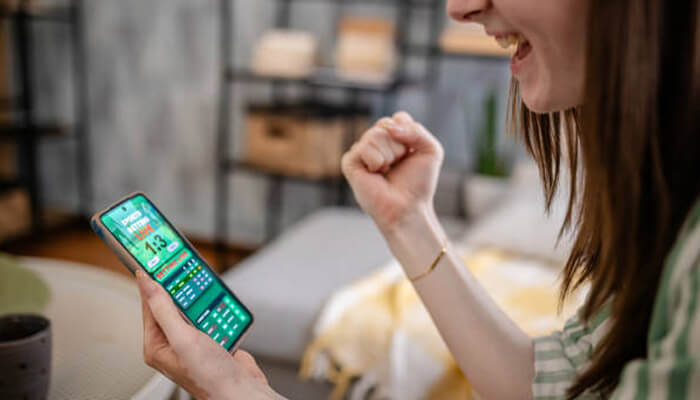 User-friendly interface and smooth navigation | tycoonstory media A woman celebrating while looking at her phone, with a visible gaming or betting app interface. The image reflects the excitement of using a platform like 1win for seamless navigation and enjoyable experiences.