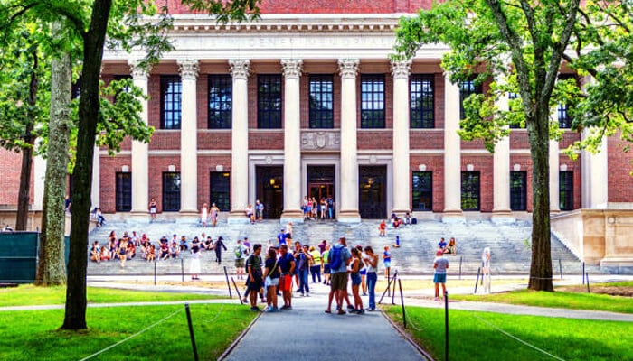 Why implementation is so complicated | tycoonstory media A university campus with students outside a grand building, highlighting the hidden infrastructure that supports education, from facilities management to complex systems.