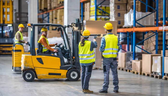 Adapting to different load types | tycoonstory media Warehouse workers using forklifts and discussing tasks, showcasing the effectiveness of modern lifting solutions for enhanced safety and efficiency.