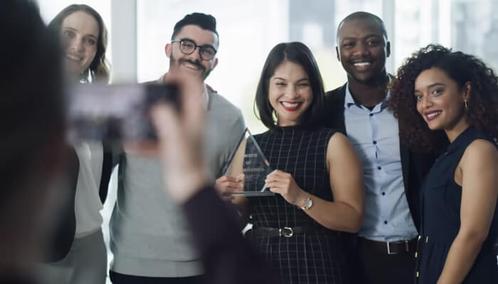 Choosing the right company awards to submit applications for | tycoonstory media A group of professionals celebrating with an award during a business event, smiling for a photo, as part of a business awards list recognition.