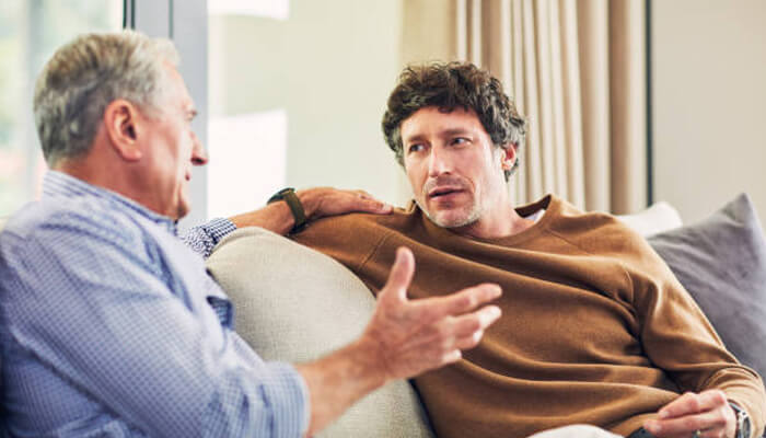 Communicating with care | tycoonstory media Two men engaging in a heartfelt conversation on a sofa, symbolizing the importance of communication during memory care and family visits.