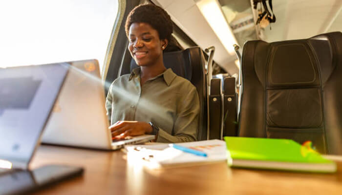 Communication and collaboration tools for work on the move | tycoonstory media A business traveller working on a laptop aboard a train, using digital tools for business travellers to stay productive while on the move.